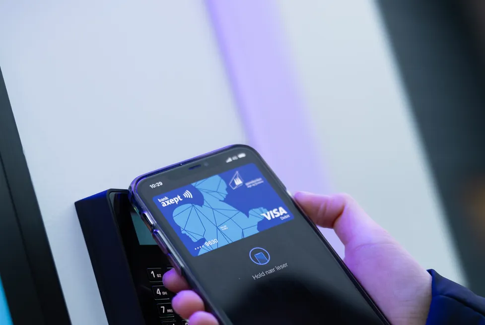 Hånd holder en mobil med Visa-kort i lommeboken mot den kontaktløse betalingsterminalen på en Vendanor-automat.