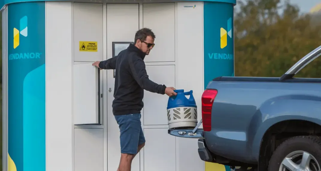 Man takes a propane cylinder from a Vendanor Propane Vending Machine and loads it onto a pickup.