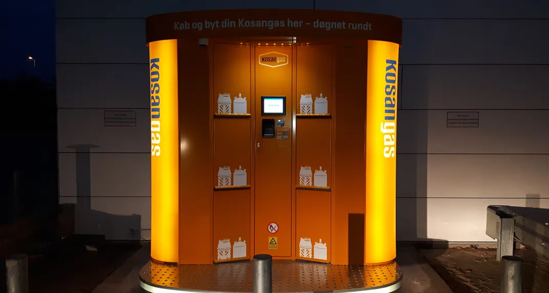Orange Kosangas Propane Vending Machine lit up at night, its doors showing cylinder graphics.