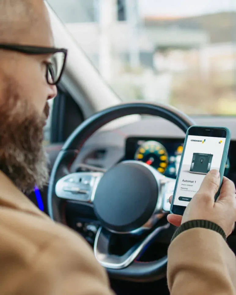 Fahrer im Auto betrachtet einen Gasflaschenautomat in der Vendanor Connect-App auf dem Smartphone.