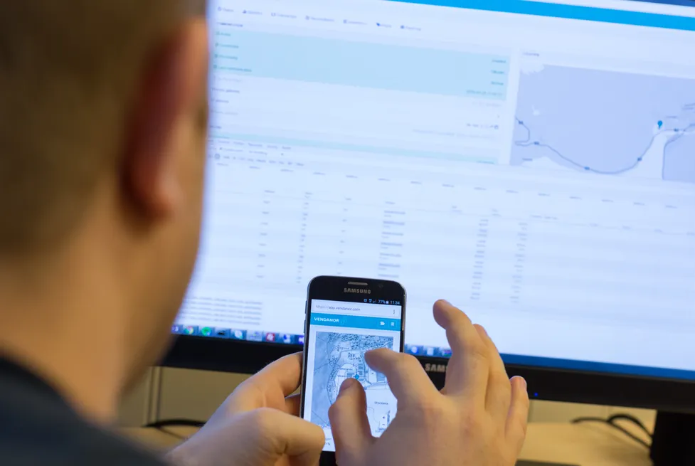 Eine Person fotografiert einen Telefonbildschirm, während das Vendanor Connect Management-Dashboard auf einem Monitor angezeigt wird.