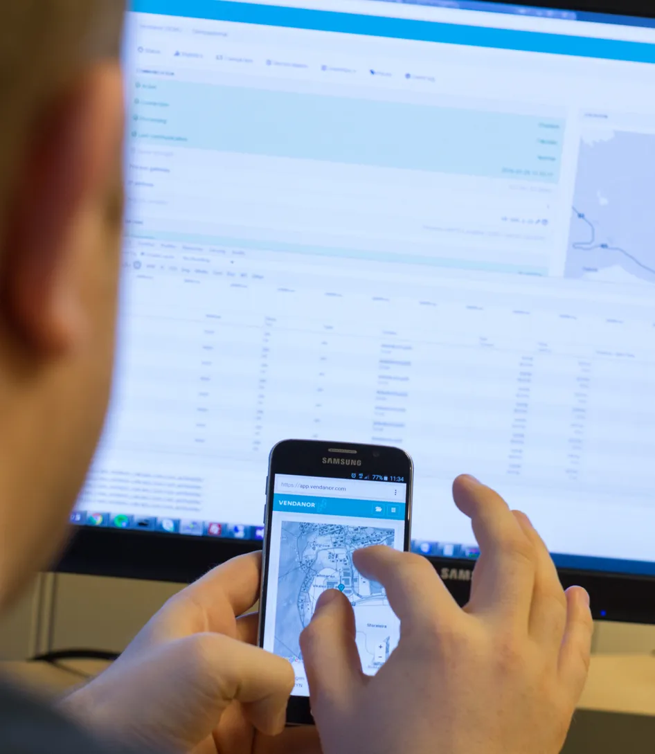 Eine Person fotografiert einen Telefonbildschirm, während das Vendanor Connect Management-Dashboard auf einem Monitor angezeigt wird.