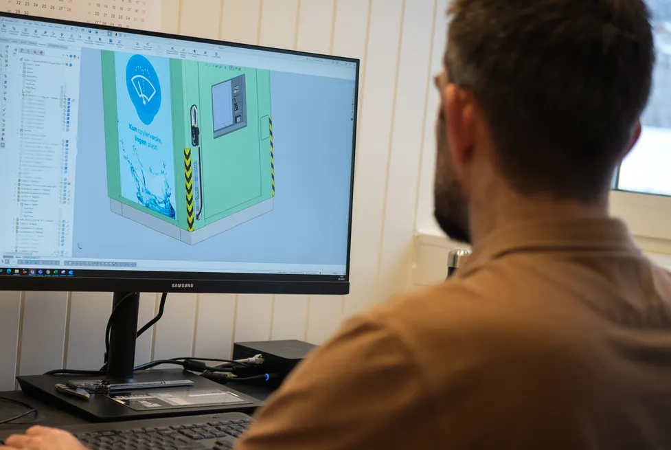 En Vendanor-ingeniør jobber ved en datamaskin som viser en CAD-modell av en Spylervæskeautomat på skjermen.