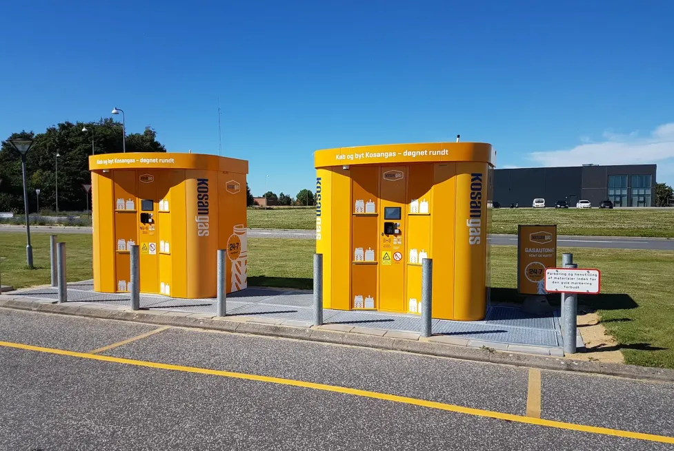 Zwei orangefarbene Kosangas Vendanor Gasflaschenautomaten an einem Außenstandort unter klarem blauem Himmel.