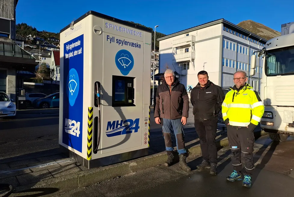 Tre menn står ved siden av en MH24-merket Vendanor Spylervæskeautomat i en gate i Måløy.