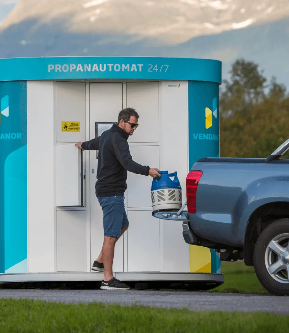 Mann lädt eine Propangasflasche aus einem Vendanor Gasflaschenautomat in einen Pickup in einer Berglandschaft.