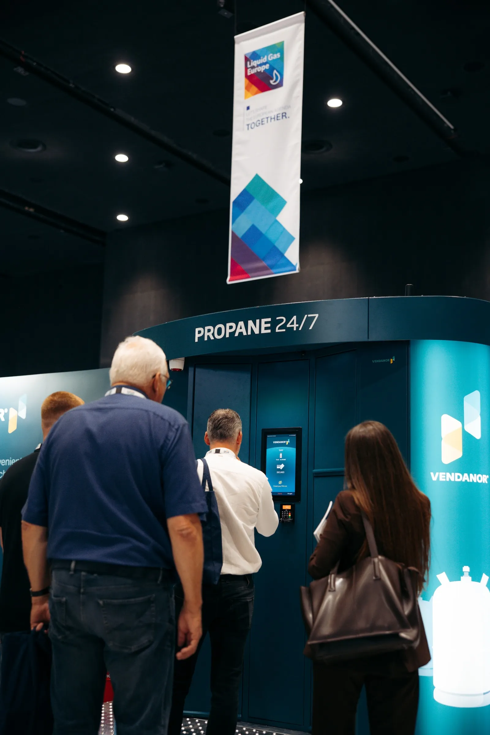 Visitors using a Vendanor Propane Vending Machine touchscreen under a Liquid Gas Europe banner at a trade fair.